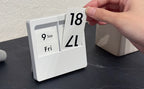 Hand changing a date panel on a white Carl Panel Calendar on a desk