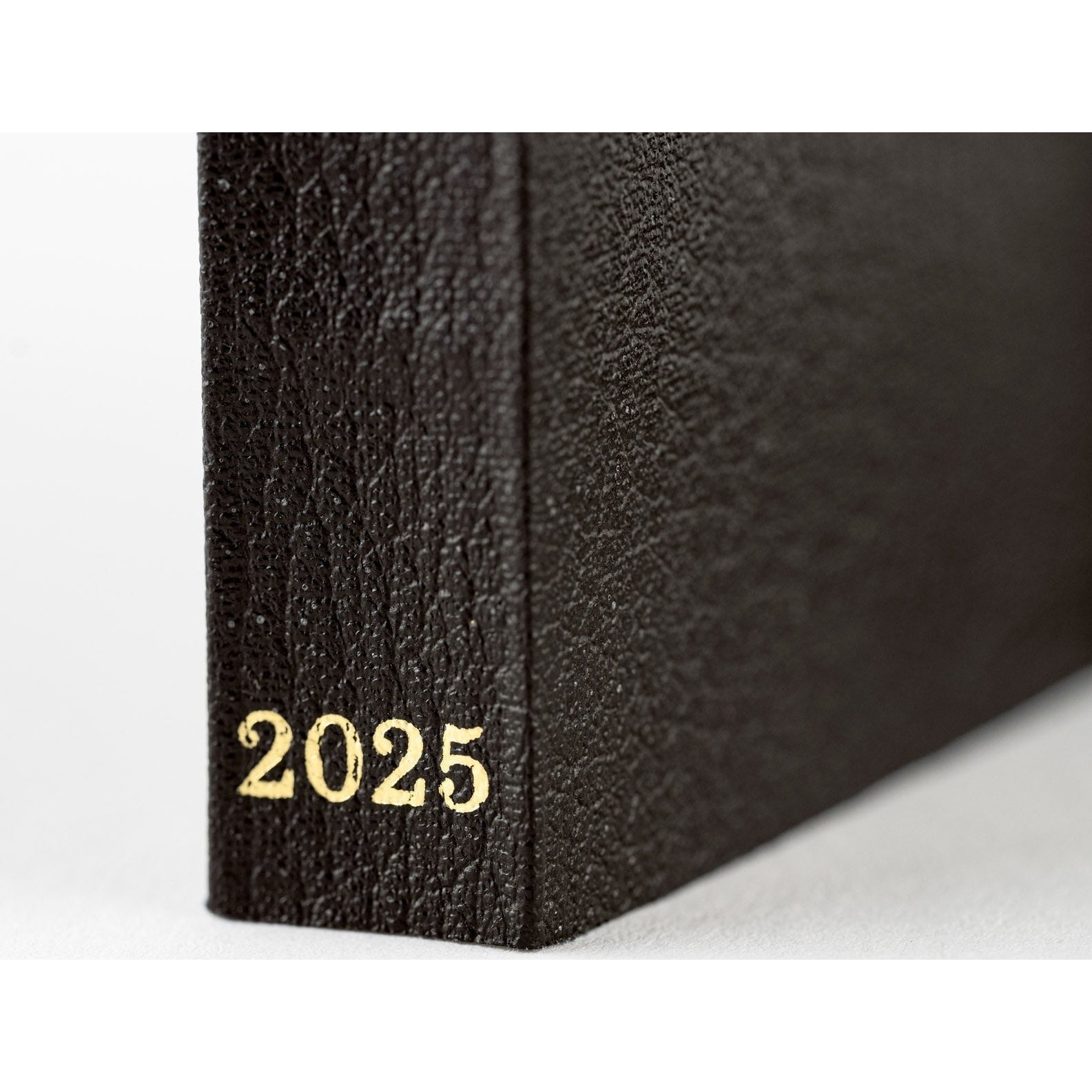 Angled close-up of black Hobonichi Techo 2025 spine showing pebbled texture and gold 2025 text
