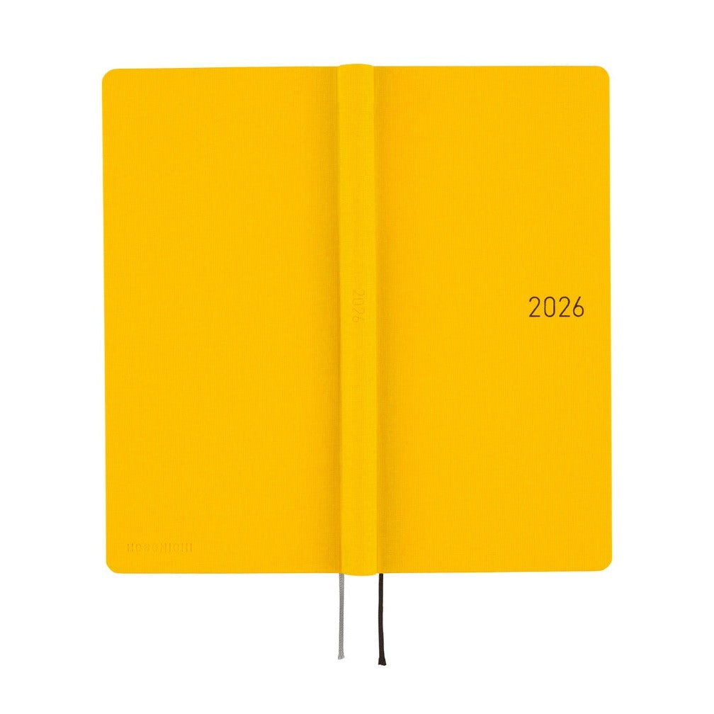 Flat lay of closed Hobonichi Techo 2026 diary showing textured yellow cover and spine detail