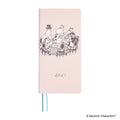 Pink hardcover Hobonichi 2027 Moomin diary showing dinner party artwork and silver foil year
