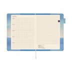 Open Hobonichi Techo A5 notebook showing grid planner pages and inner flap sunrise seascape artwork