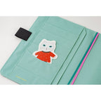 Close-up of mint green pocket in Hobonichi A5 cover featuring die-cut cat sticker and Yumi Kitagishi branding