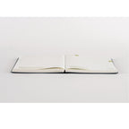 Hobonichi Techo A5 2025 diary open on white surface showing dark navy cover and gold-edged off-white grid pages