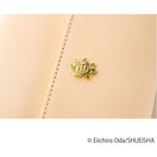 Macro shot of smiling sun face pin attached to textured beige One Piece notebook cover