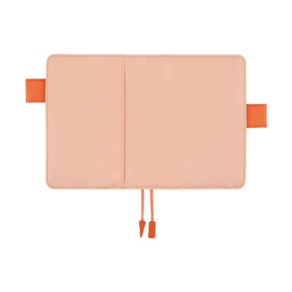 Flat lay of closed pink Hobonichi A6 planner cover with dual orange clasps and ribbon tie
