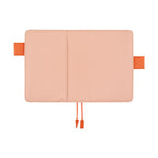 Flat lay of closed pink Hobonichi A6 planner cover with dual orange clasps and ribbon tie
