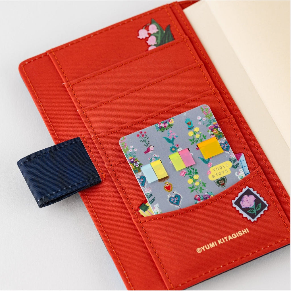 Gray floral sticky note holder inside orange fabric pocket organizer with Yumi Kitagishi branding
