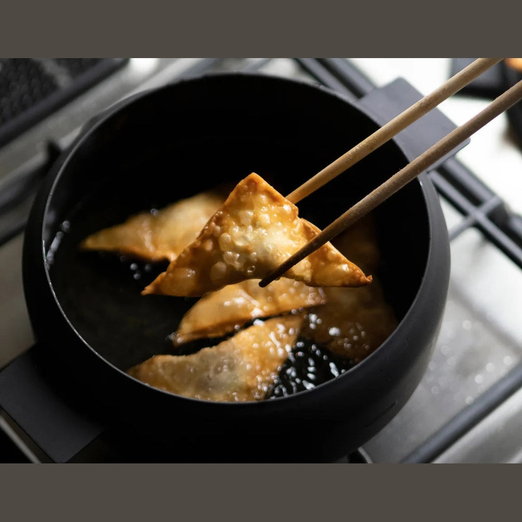Black iron deep frying pot cooking triangular fried items in oil
