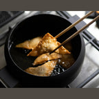 Black iron deep frying pot cooking triangular fried items in oil