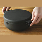 Hands placing black iron deep fryer lid onto matching pot