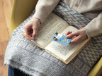 Person using blue penguin card sticky notes as bookmarks in an open book
