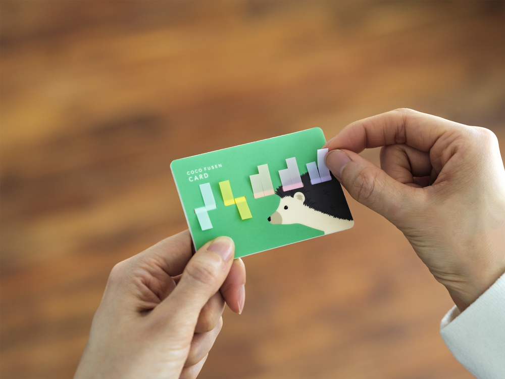 Close-up of green hedgehog card sticky note case with finger peeling purple tab