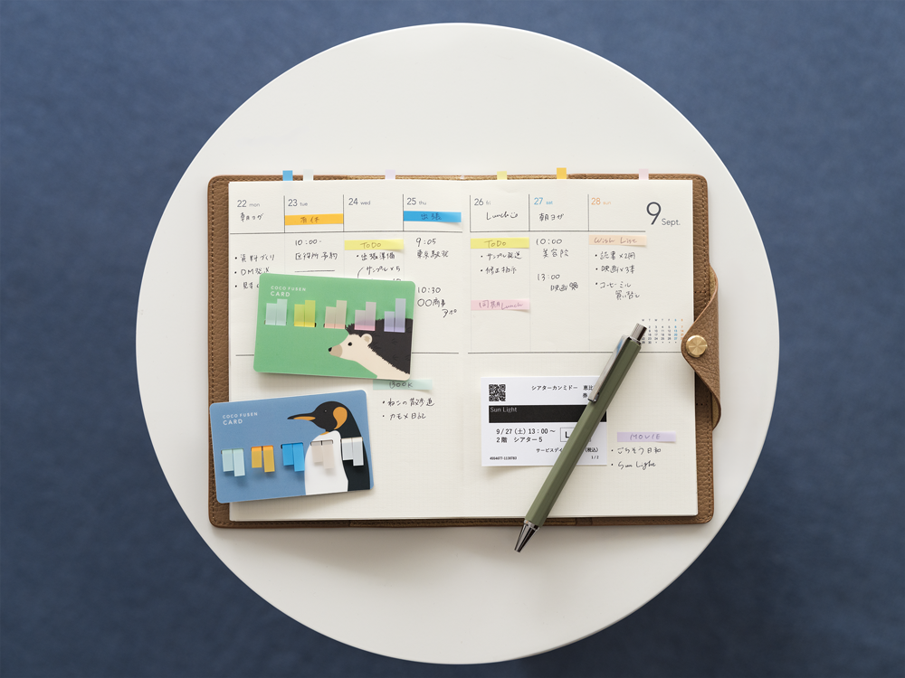 Weekly schedule marked with colorful sticky notes in leather planner with hedgehog and penguin holders