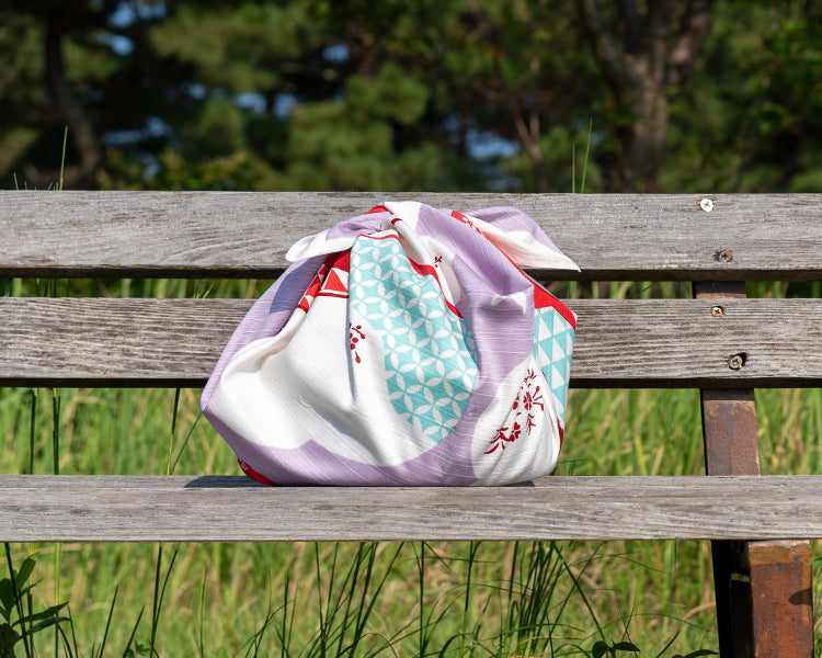 Pink Ume Docho Furoshiki cloth tied in pouch style on wooden bench highlighting patchwork triangle details