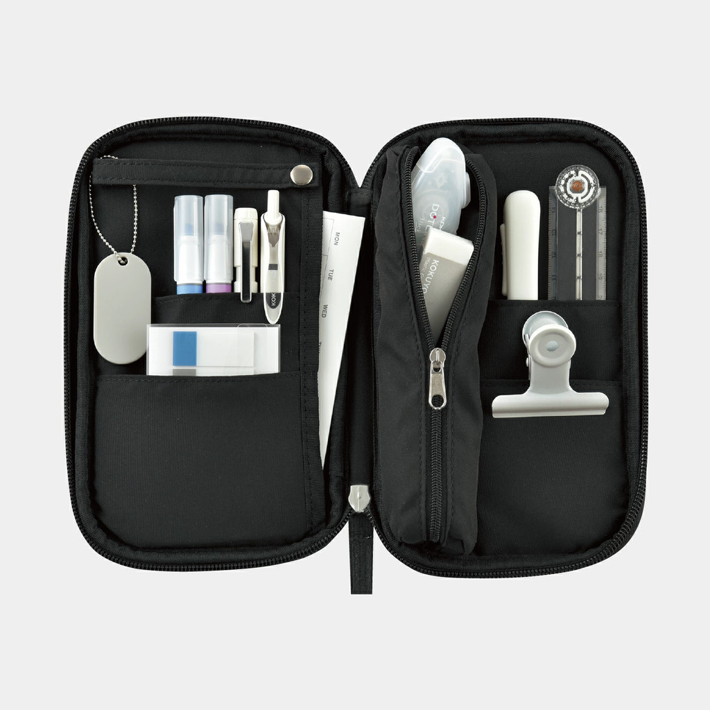Open black Kokuyo Pancase pencil case with dual panels holding pens, compass, and dog tag chain