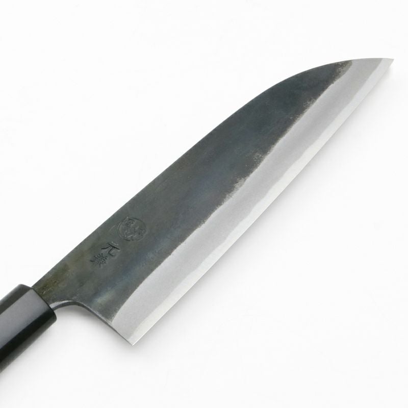 Macro detail of Motokane Santoku knife tip, kurouchi texture, and stamped logo