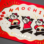 Angled view of red postcard with shiny gold foil stamped characters and scalloped border design