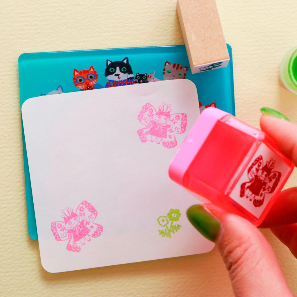 Hand stamping pink butterfly design on teal cat supper stamp mat with green nail polish