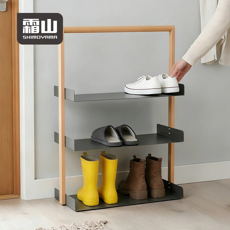 Lifestyle shot of three-tier shoe rack holding sneakers, slippers, and boots in an entryway with light wood frame