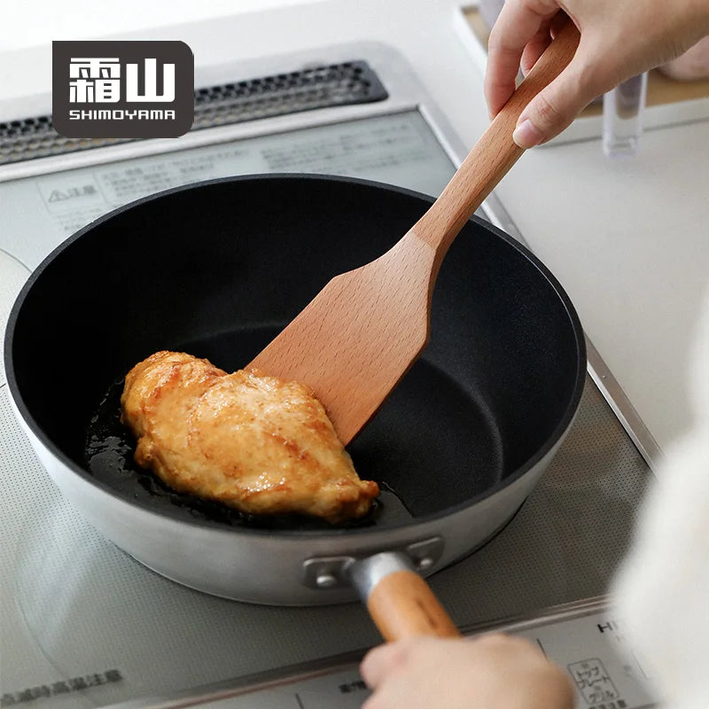 Sliding square beech spatula under chicken breast in frying pan