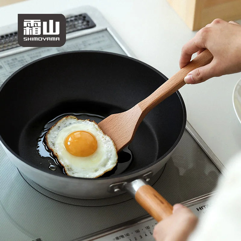 Square beech spatula lifting fried egg from non-stick skillet