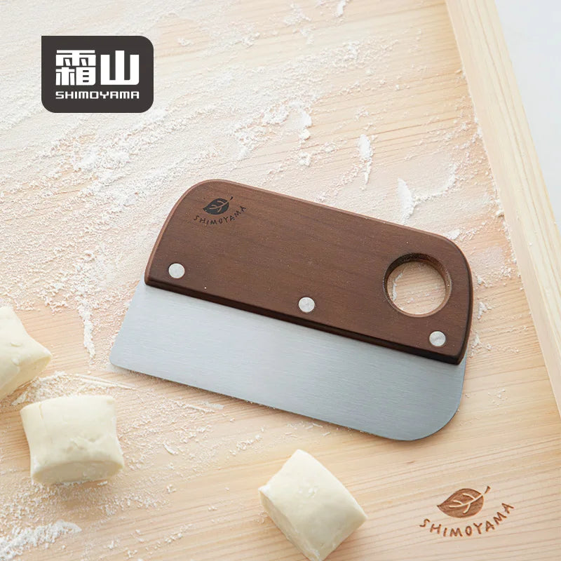 Shimoyama cherry wood dough scraper lying on floured board with laser-engraved leaf logo