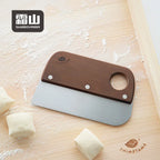 Shimoyama cherry wood dough scraper lying on floured board with laser-engraved leaf logo