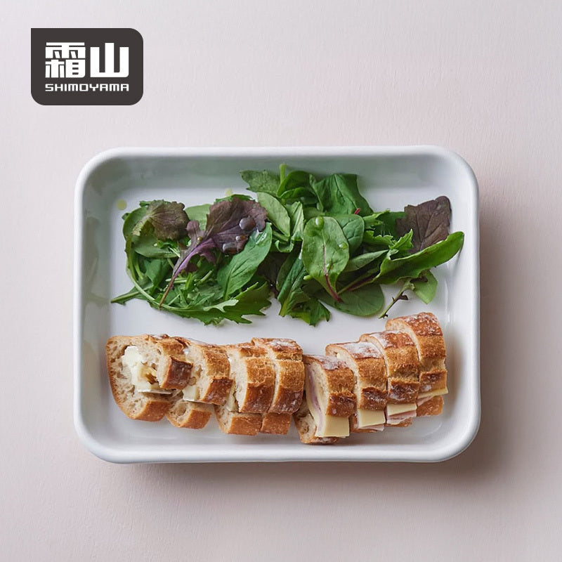 White enamel prep tray holding salad and baguette sandwiches