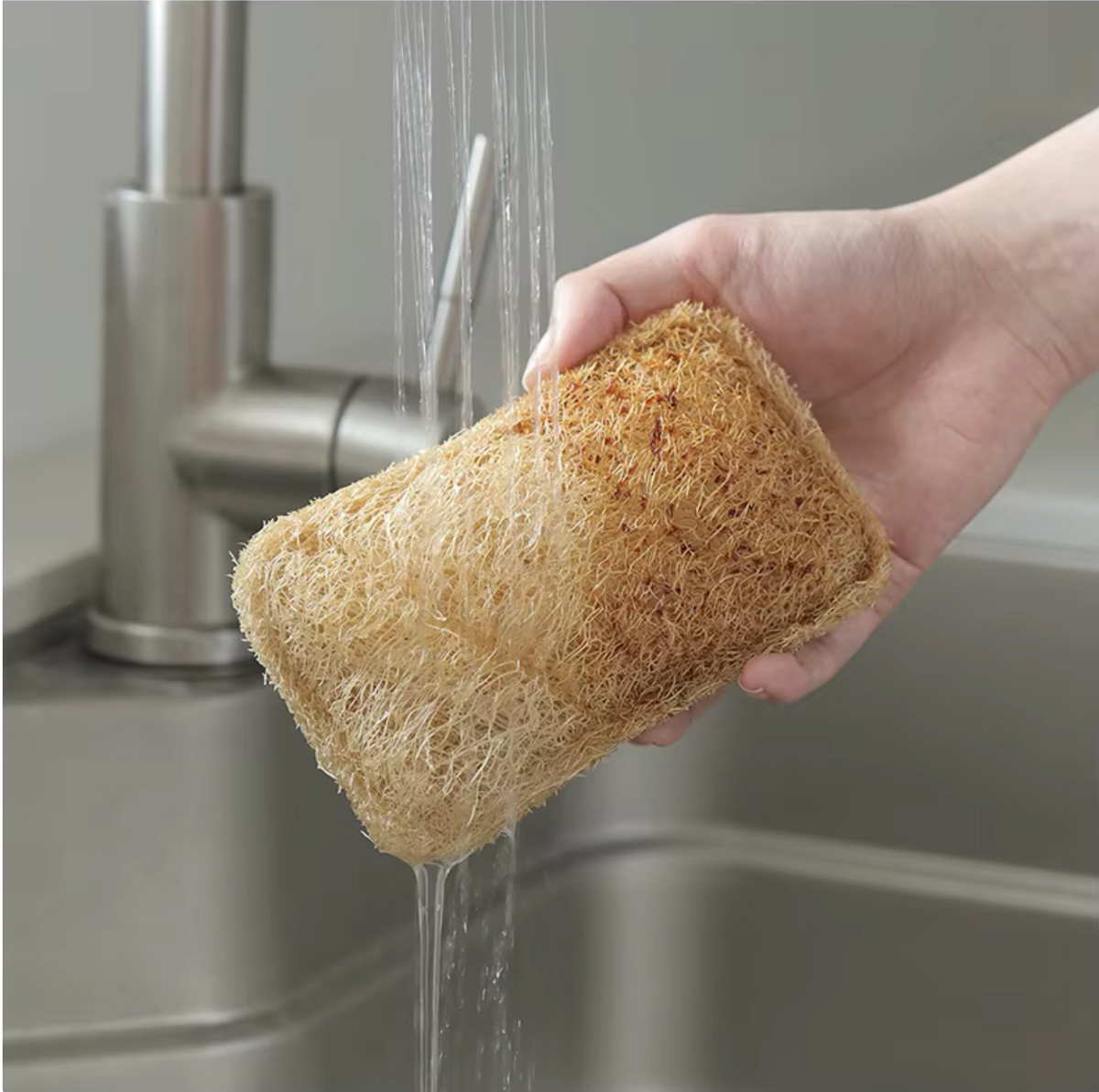 Wet natural loofah scrubber softening under running water in sink