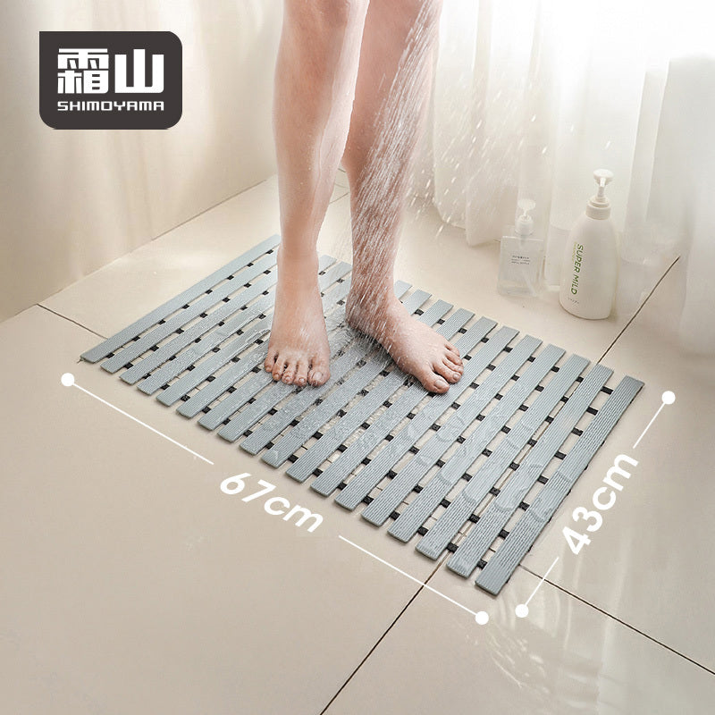 Bare feet on grey non-slip bath mat under running water, showing 67x43cm size