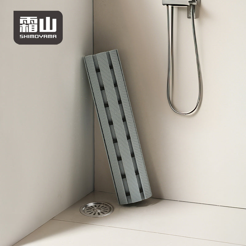 Rolled grey PVC bath mat leaning against shower wall, demonstrating compact storage