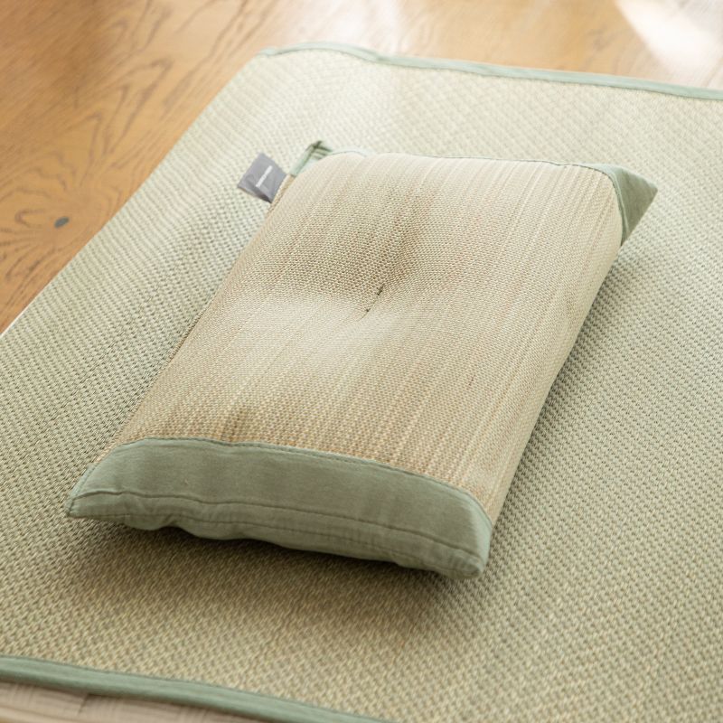 Olive green cotton trimmed rush straw pillow resting on matching mat