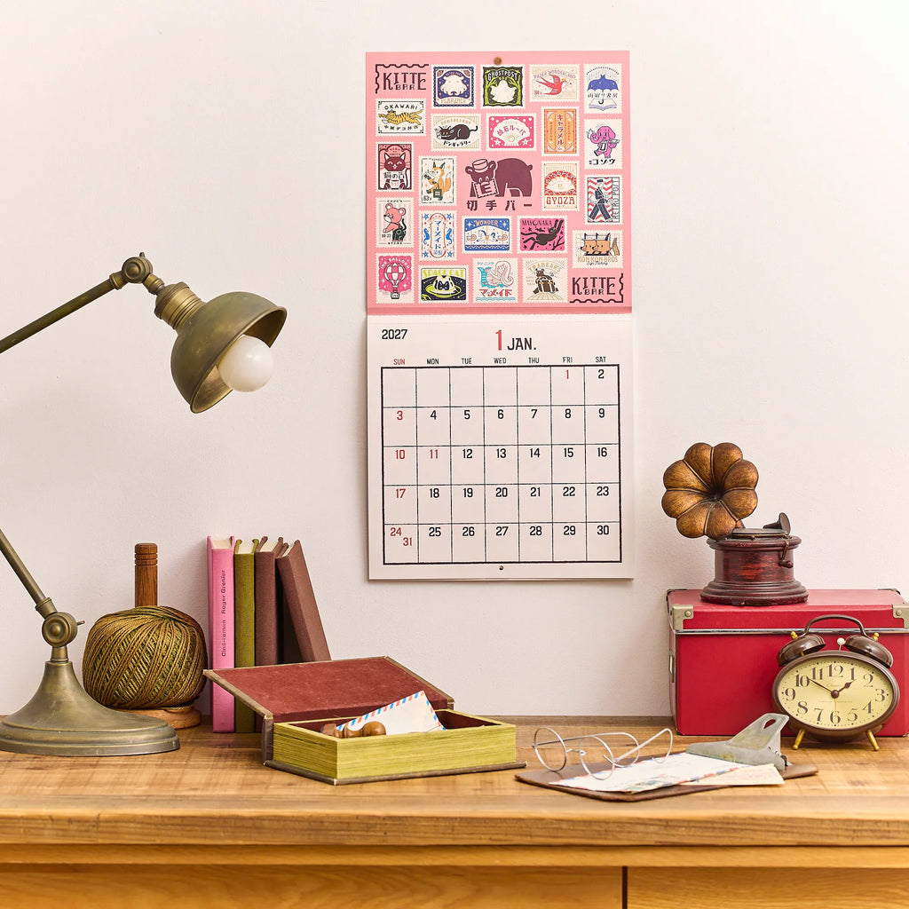 ob1toy LP Wall Calendar 2027 hanging on a wall above a desk and lamp