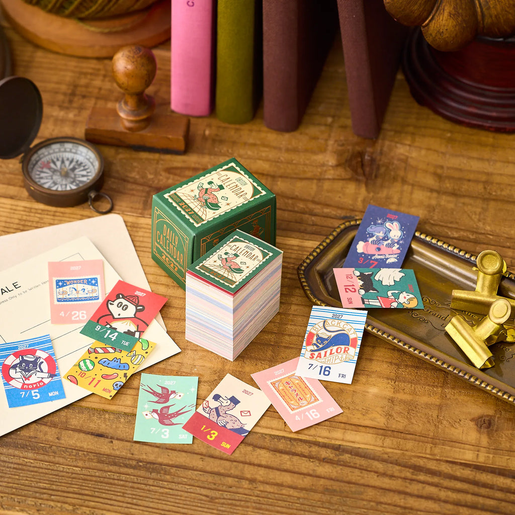 ob1toy Mini Daily Calendar 2027 on a wooden desk with torn-off sheets around it