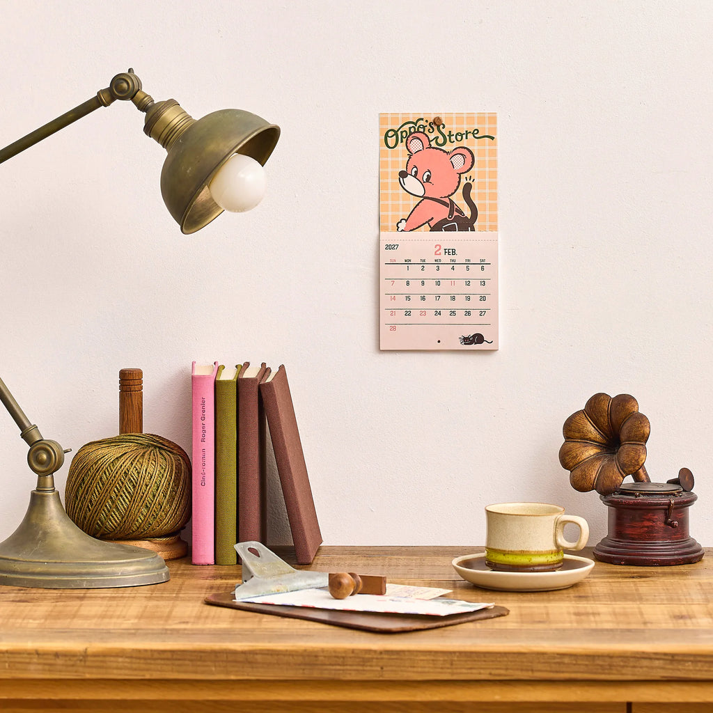 ob1toy Mini Wall Calendar 2027 hanging on a wall above a desk and lamp
