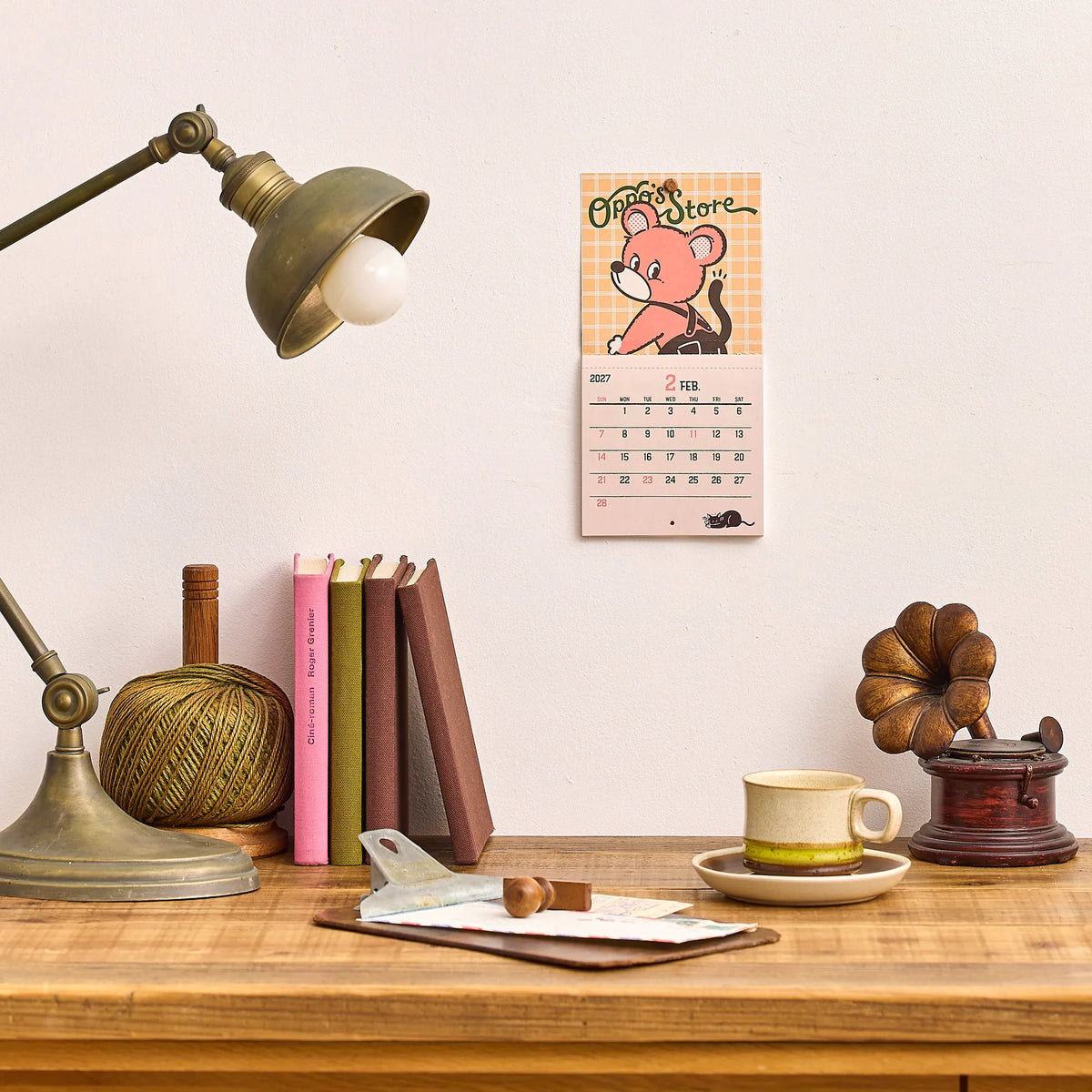 ob1toy Mini Wall Calendar 2027 hanging on a wall above a desk and lamp