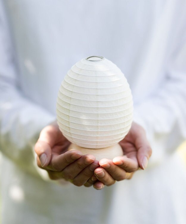 Hand holding small white egg chochin lantern showing bamboo frame detail and wood base