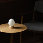 Miniature egg-shaped paper lantern on wooden base styled in dimly lit room setting