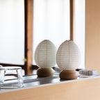 Two unlit Shiraki egg paper lanterns with wooden bases displayed side by side