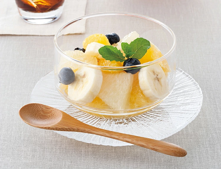 Close up of clear glass canister holding fresh fruit salad and mint leaves