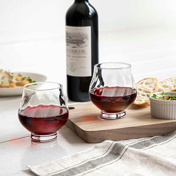 Faceted stemless wine glasses on wooden board with bread and wine bottle