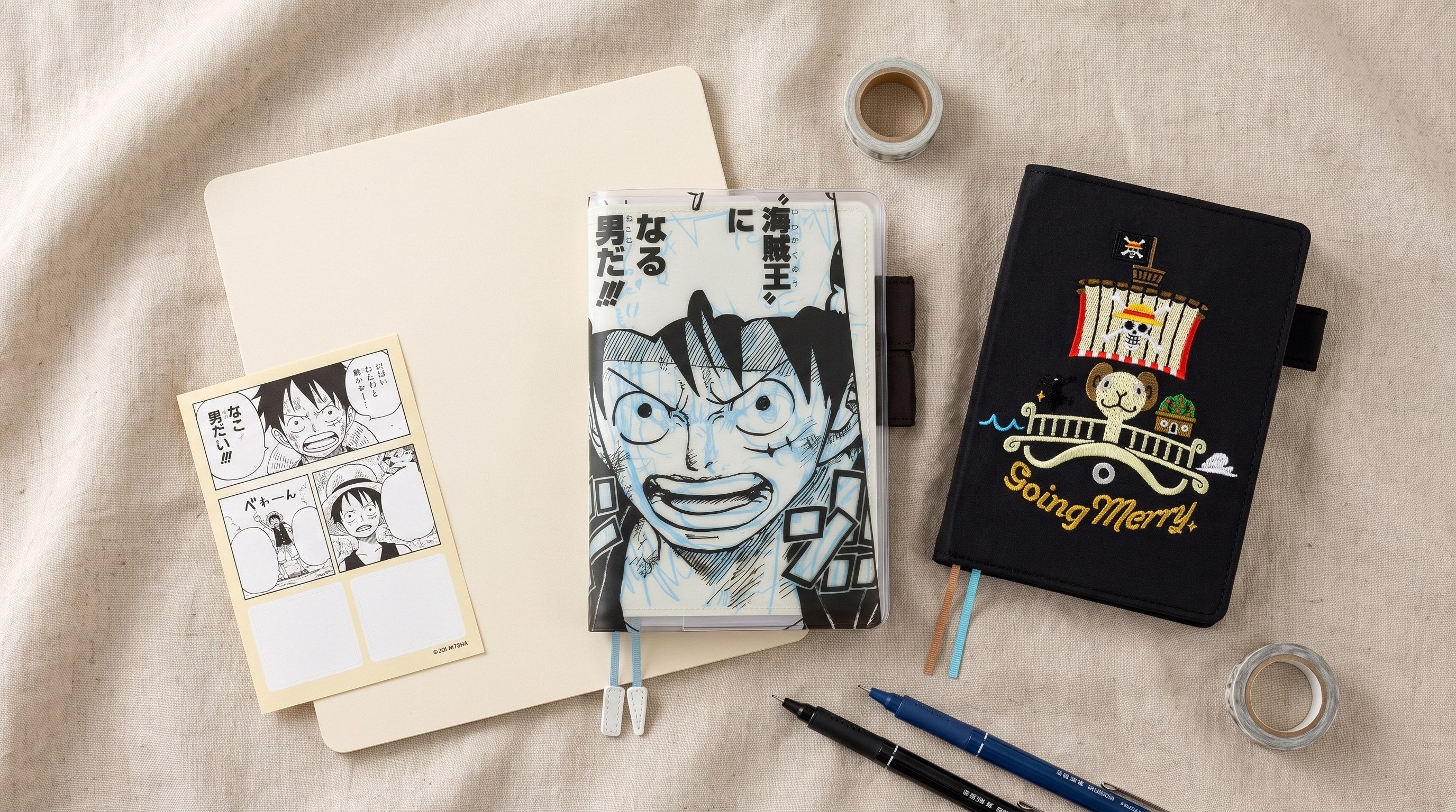 Hobonichi Techo ONE PIECE magazine collaboration flat lay: Episode 1000 cover, embroidered Going Merry cover, pencil board and stationery on linen