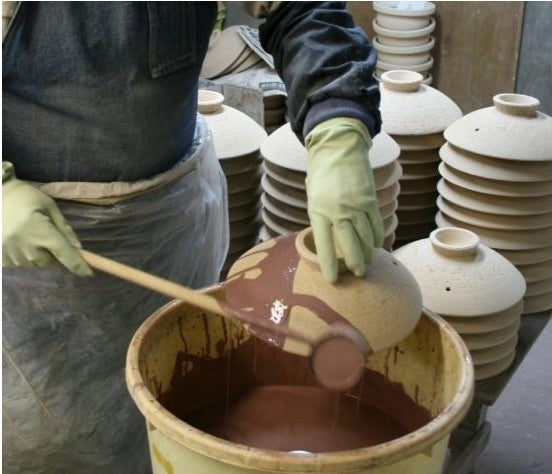 A potter dipping a donabe lid into a tub of glaze