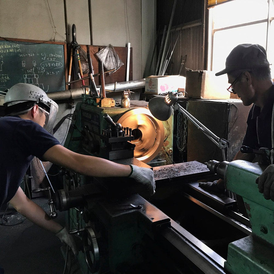 Two workers at a metal-spinning lathe on the factory floor