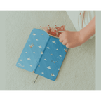 Blue fabric One Piece diary on carpet with toy sailboat and ribbon bookmark