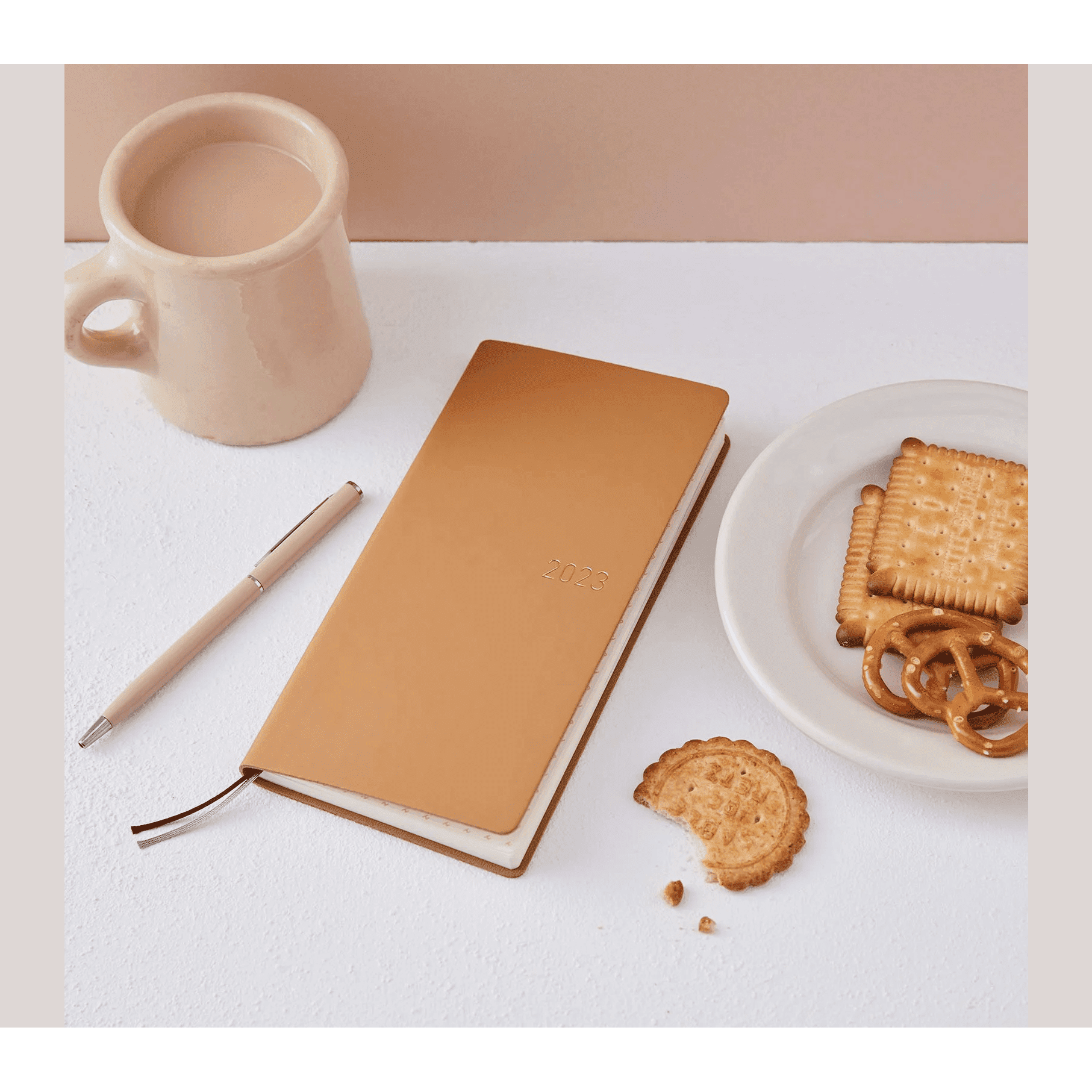 Diagonal tan Hobonichi Techo 2023 planner with beige pen and snack props