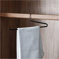 Single black minimalist anti-slip trouser hanger suspending gray pants from wooden rod